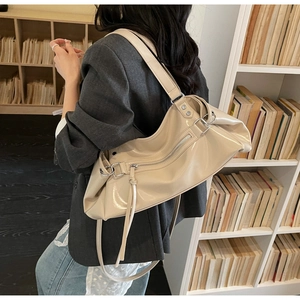 Detail of beige patent leather shoulder bag with decorative tassels and wide strap