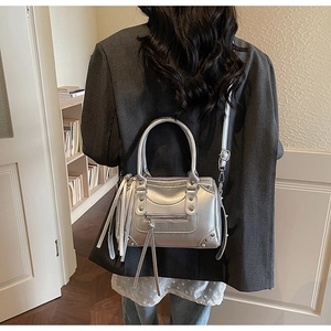 Silver metallic crossbody bag with rivets and long tassels shown on shoulder