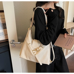 Sac fourre-tout beige en similicuir avec boucle dorée porté par un mannequin en extérieur