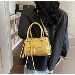 Detail of yellow rivet Boston bag with tassels on a model in a stylish interior