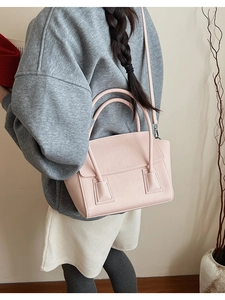 Pale pink leather trapezoid handbag worn crossbody with casual grey sweatshirt and white shorts