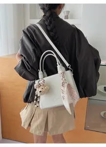 White leather handbag with scarf handle and bear charm shown on a model's shoulder