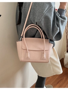 Detail of a minimalist pink leather crossbody bag with dual handles on a female model