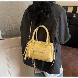 Detail view of bright yellow studded Boston bag with long tassels on a crossbody strap