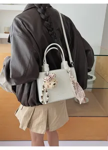 Detail of cream white faux leather handbag with lychee texture and plush bear pendant