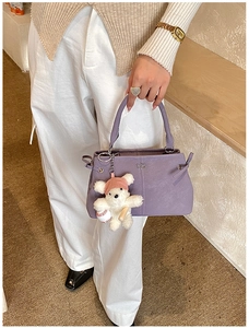 Detail of purple leather handbag featuring a plush bear charm and metallic logo accents