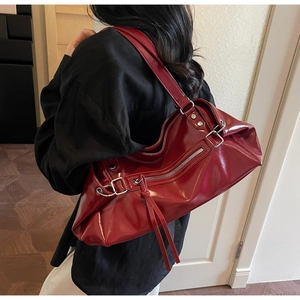 Detail of burgundy patent leather tote with silver zippers and long tassels on model