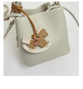 Detail of grey lychee leather bucket bag featuring a colorful rocking horse charm
