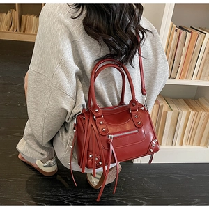 Macro view of dark red leather handbag featuring metallic studs and tassel details