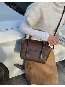 Minimalist dark brown leather trapezoid handbag worn by model in urban street setting