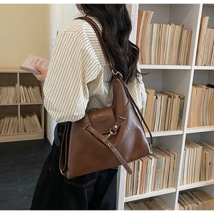 Détail du sac bandoulière vintage marron foncé avec boucles dorées dans une librairie