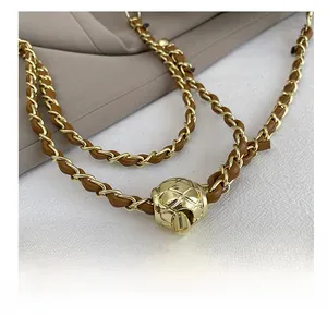Detail of gold metal chain woven with brown leather and adjustable quilted ball buckle