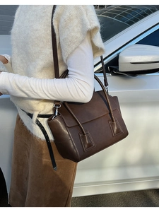 Detail of dark brown leather crossbody bag with flap design and metal hardware on street