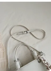 Detail of adjustable leather shoulder strap and metallic buckle on a white handbag