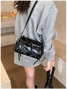 Detail of a shiny black moto-style shoulder bag with silver studs and zipper accents