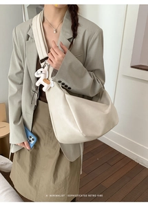 Detail of minimalist cream hobo bag with wide shoulder strap and horse charm