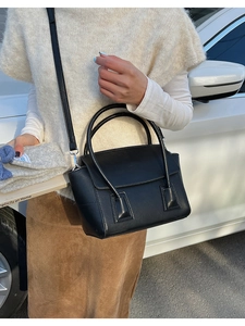Detail of minimalist black leather trapezoid bag with dual handles and slim shoulder strap