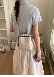 Detail of a beige leather bucket bag featuring a unique braided handle and textured finish