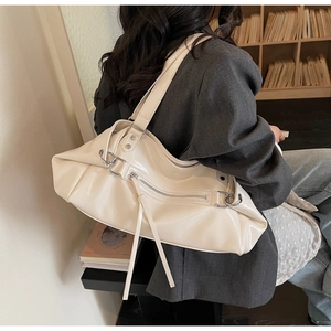 Detail of cream shoulder bag featuring silver rivets, metal rings and long leather tassels