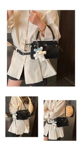 Detail of black matte leather tote bag with white bear pendant and adjustable strap
