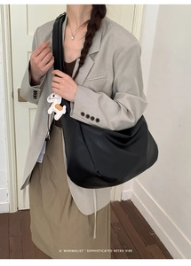Close-up of a large black tote bag with a white horse charm on a grey suit model