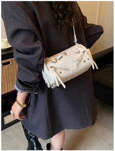 Detail view of cream barrel bag with metallic zippers and studs on shoulder strap