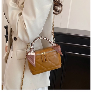 Close-up of brown quilted handbag with silk scarf detail and metal chain strap