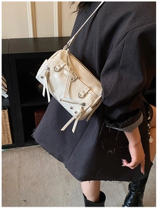 Detail of cream biker crossbody bag with decorative metal zippers and long tassels