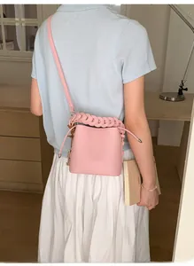 Detail of pink drawstring bucket bag featuring lychee texture leather and woven handle