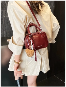 Détail du sac bandoulière en cuir verni bordeaux avec breloque ours sur le mannequin