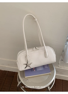 Detail of white baguette bag with silver star charm and double zipper on leather texture