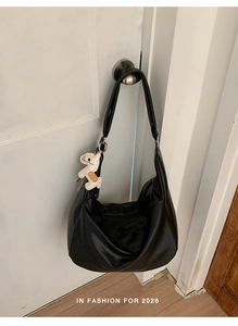 Detail of a black hobo bag with a leather horse charm hanging from the wide shoulder strap