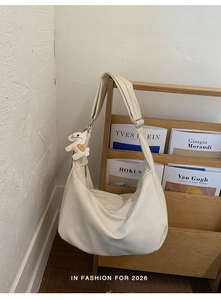 Detail of cream pleated shoulder bag with a cute white rabbit pendant on a wooden rack