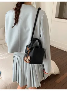Detail of black lychee grain bucket bag with woven handle and wooden pony charm on model