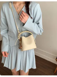 Detailed shot of beige bucket bag with woven handle and wooden charm on model
