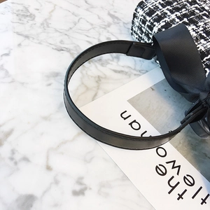 Elegant tweed plaid crossbody bag with a chic black bow decoration on white marble