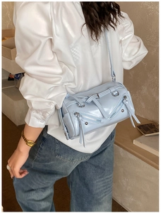 Detail view of a light blue cylinder pillow bag with decorative zippers and silver hardware
