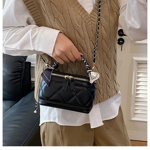 Macro view of black quilted leather mini bag with silk scarf handle and gold chain strap