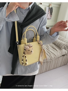 Close-up of pale yellow PU handbag with silk scarf handle and cute teddy bear pendant