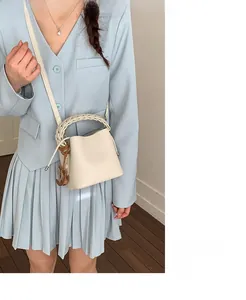 Detail of light beige bucket bag with woven handle shown on model in a blue suit