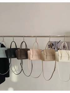 Detail view of various minimalist leather crossbody bags in pastel colors hanging on a rack