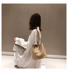 Vue détaillée du sac seau beige minimaliste avec étiquette assortie porté par un mannequin