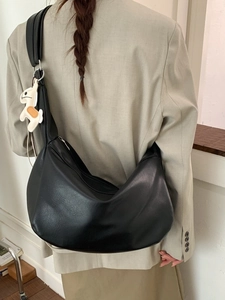 Minimalist black crescent crossbody bag with cute dog charm on a light suit model