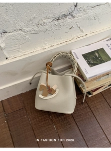 Close-up of cream-white bucket bag with braided handle and wooden rocking horse charm
