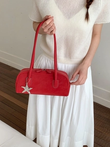 Minimalist red leather bowling bag with star pendant shown on a model in a modern room