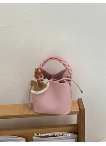 Detail of pink lychee leather bucket bag with braided handle and wooden pony charm