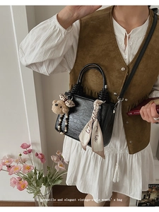 Detail of black glossy leather handbag with brown plush bear charm and printed silk scarf