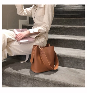 Sac seau en cuir marron avec large bandoulière posé sur des marches en pierre naturelle