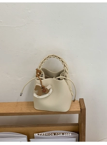 Detail of cream drawstring bucket bag with woven handle and wooden horse charm
