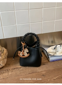 Close-up of black lychee grain bucket bag with woven handle and wooden horse charm